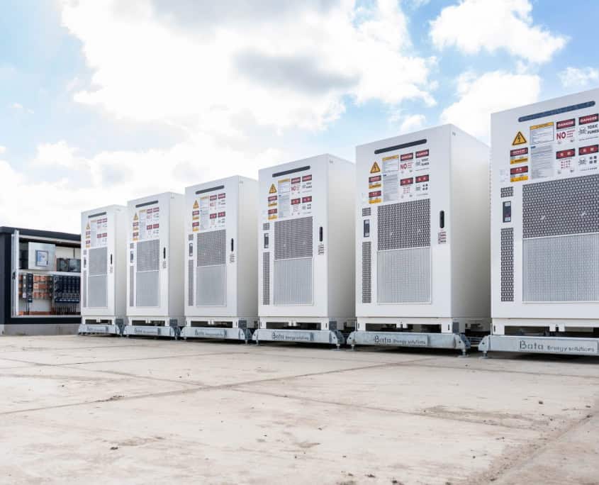Een rij witte industriële batterijopslagunits staat op een betonnen ondergrond onder een bewolkte hemel. Het is onderdeel van het indrukwekkende project met zes stations dat in productie is voor Privatis Infrabeheer Zwolle.