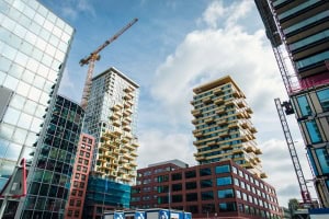 Moderne hoogbouw en een bouwkraan rijzen op naast een transformatorstation, tegen een gedeeltelijk bewolkte lucht in een stedelijk landschap in ontwikkeling.