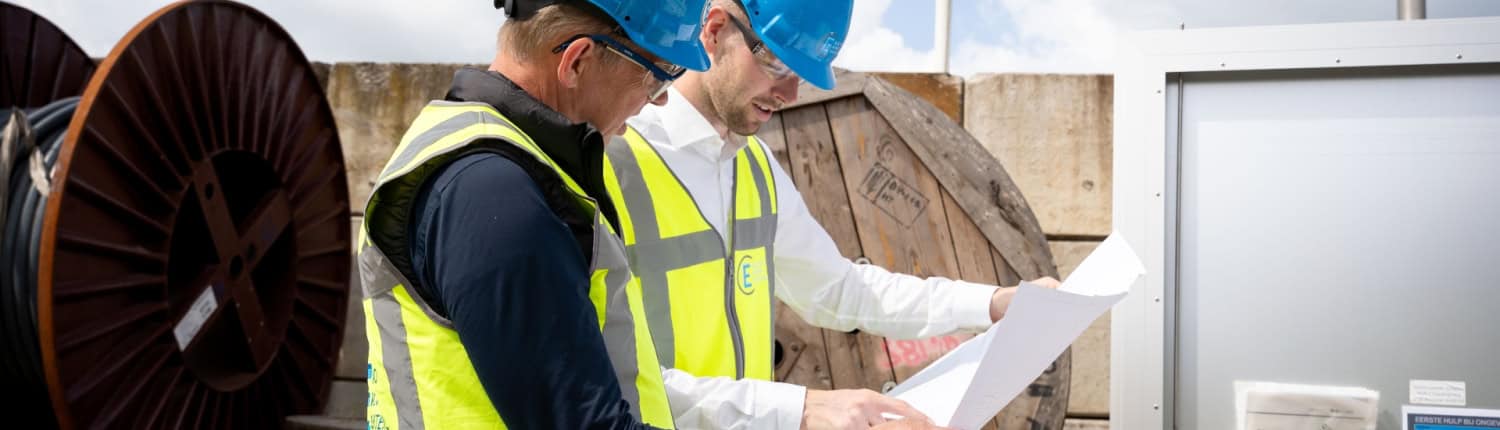 Twee bouwvakkers met blauwe helmen en gele veiligheidsvesten bekijken blauwdrukken op een buitenwerkplek in de buurt van kabelhaspels en apparatuur van Electro Power Systems.