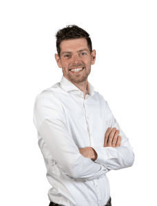 Een man met kort bruin haar en een baard, die een wit overhemd draagt, staat met gekruiste armen en glimlachend tegen een effen witte achtergrond.