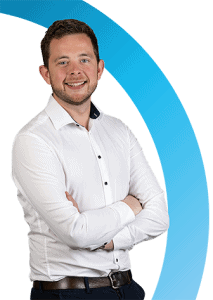 Een man in een wit overhemd en donkere broek staat met gekruiste armen te glimlachen voor een witte achtergrond met een blauwe gebogen afbeelding.