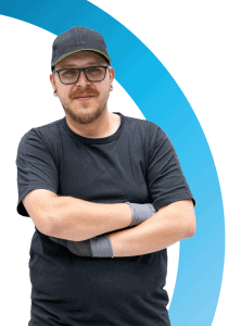 Man met zwart t-shirt, pet en bril staat met gekruiste armen voor een witte achtergrond met een blauw gebogen ontwerp, perfect voor een introductie van een 