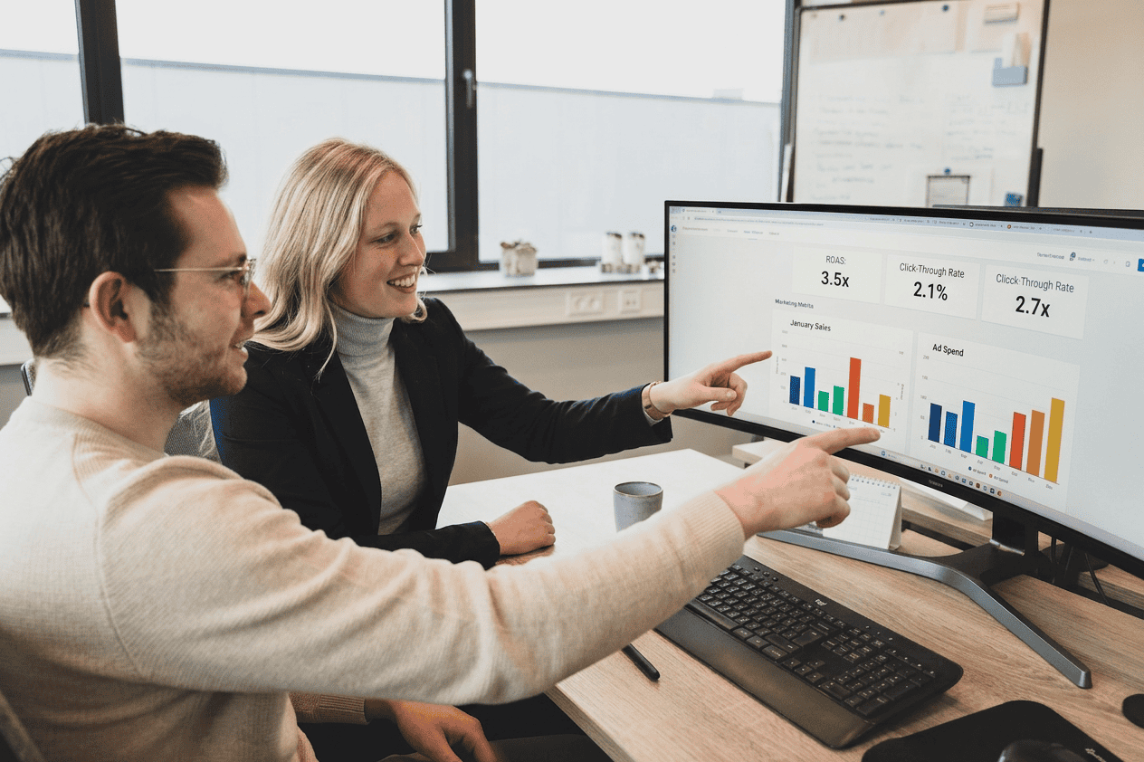 Twee mensen zitten aan een bureau en bespreken staafdiagrammen en prestatiecijfers op een computerscherm in een kantoor – een kijkje in de samenwerkingsomgeving wanneer je bij Electro Power Systems werkt.